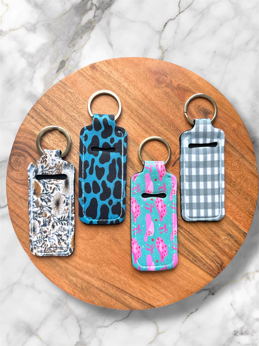 Four chapstick holder keychains with different patterns on a wooden round board.