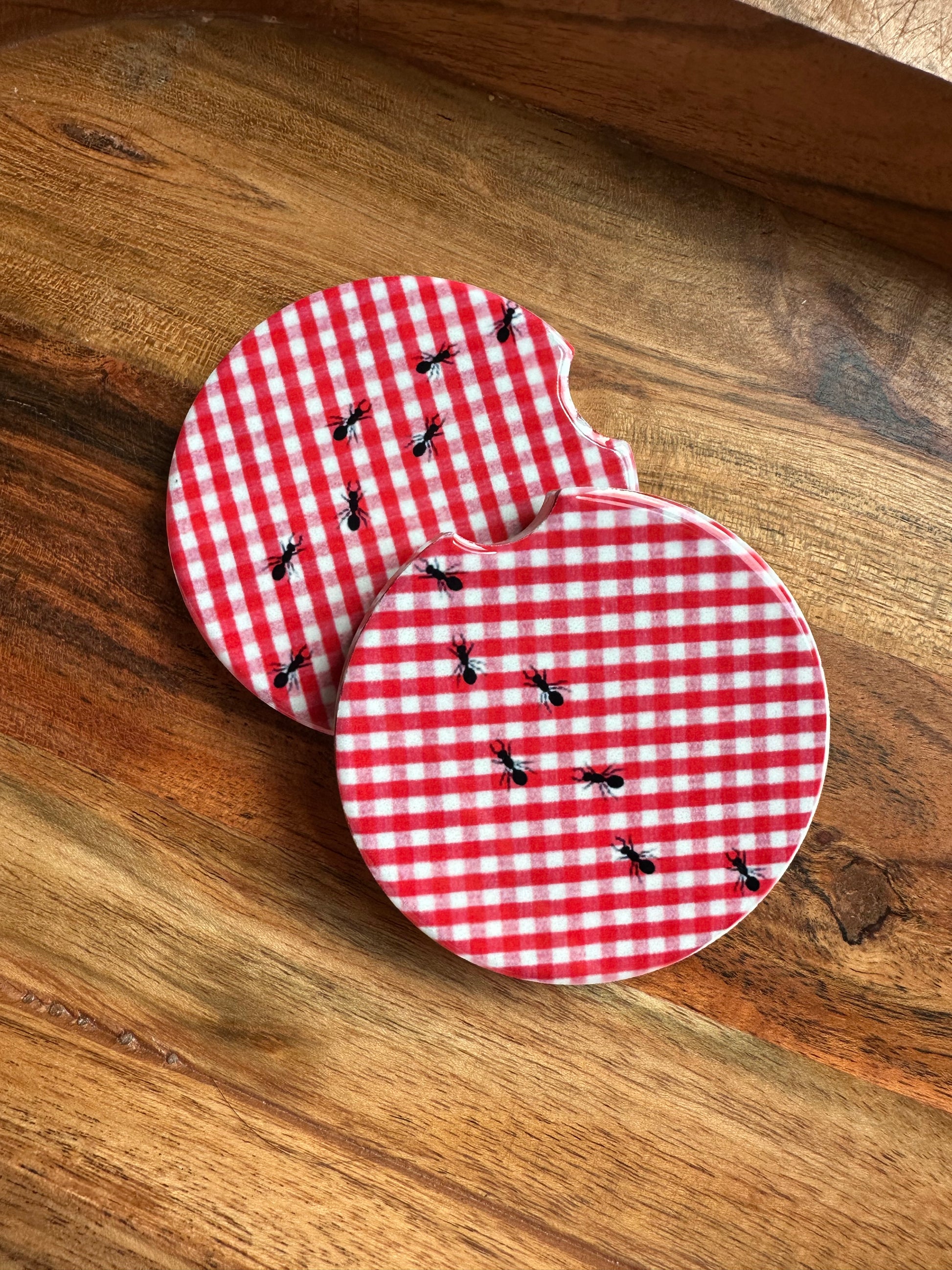 red and white gingham print picnic basket with ants ceramic car coasterstacked on wooden background