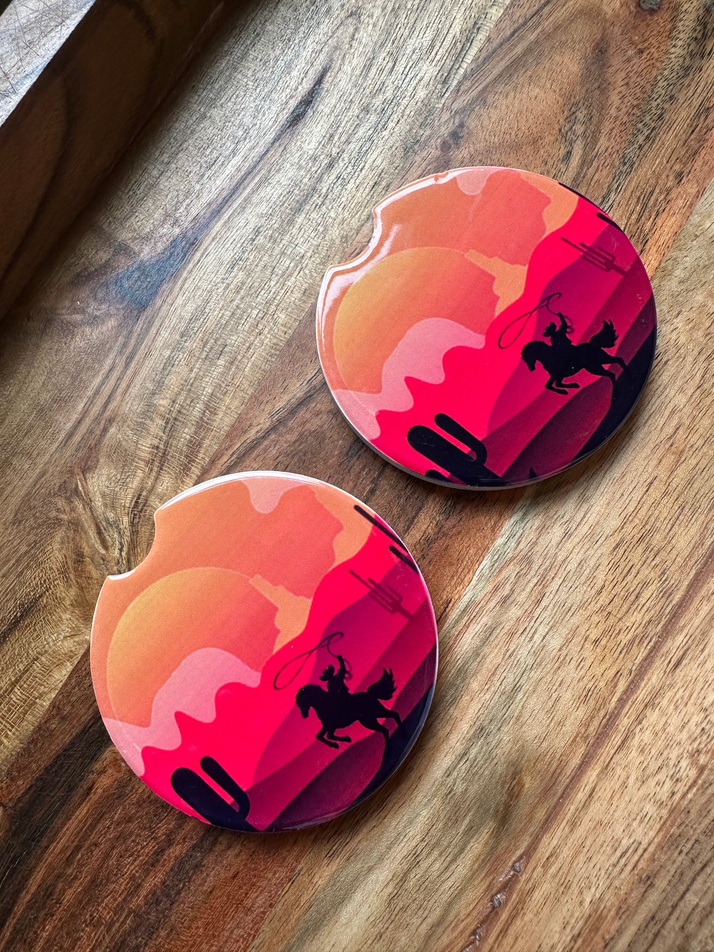cowboy in a desert sunset ceramic car coaster on a wooden background