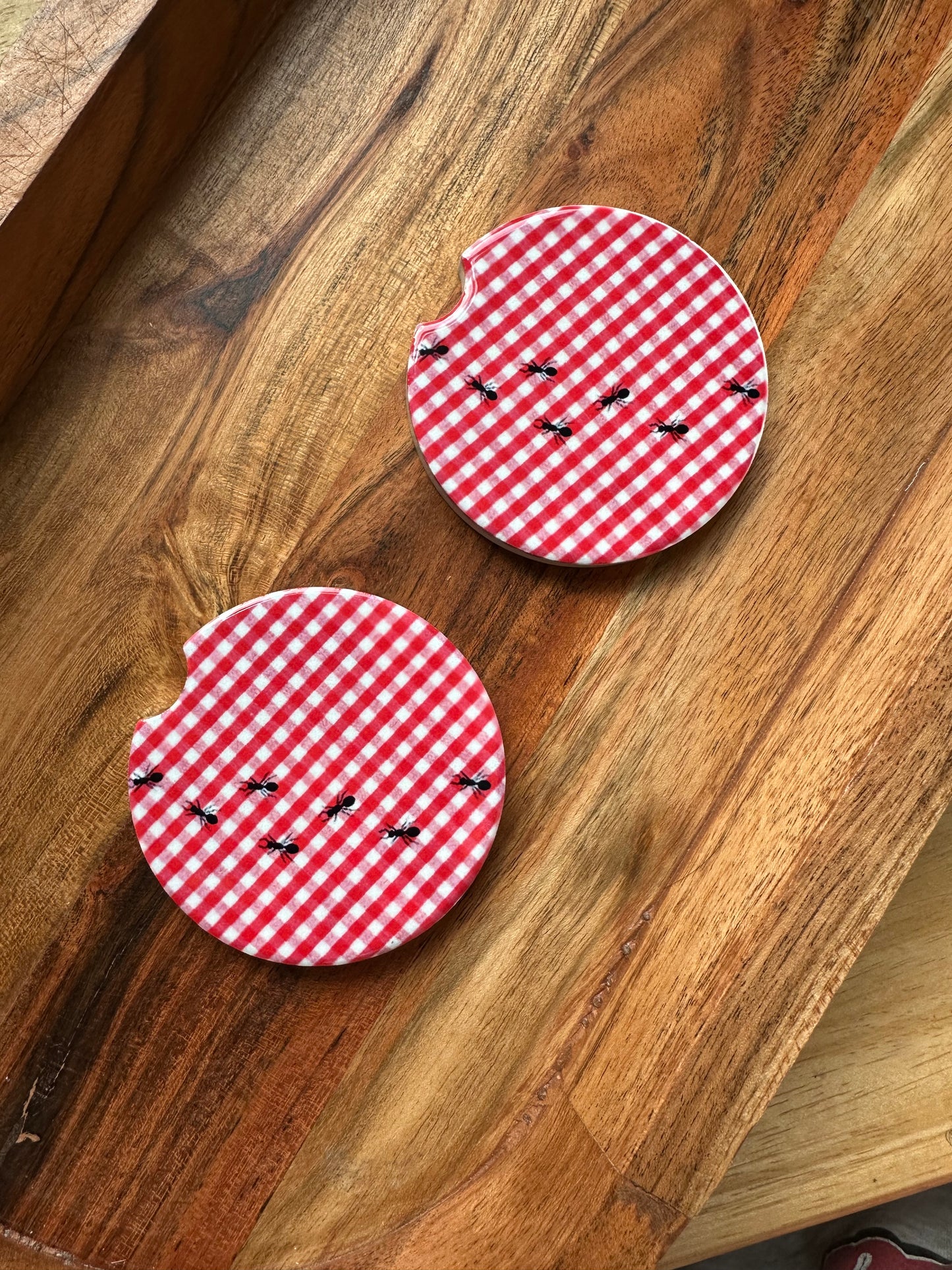 red and white gingham print picnic basket with ants ceramic car coaster on wooden background