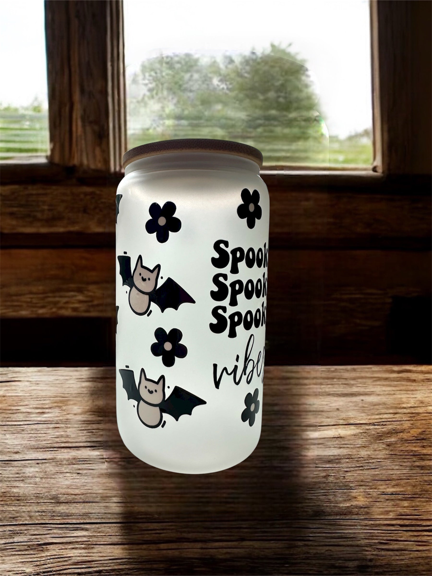Frosted glass can-shaped tumbler with Halloween-themed design that says 'spooky spooky spooky vibes' on the front, sitting on top of a wooden surface.
