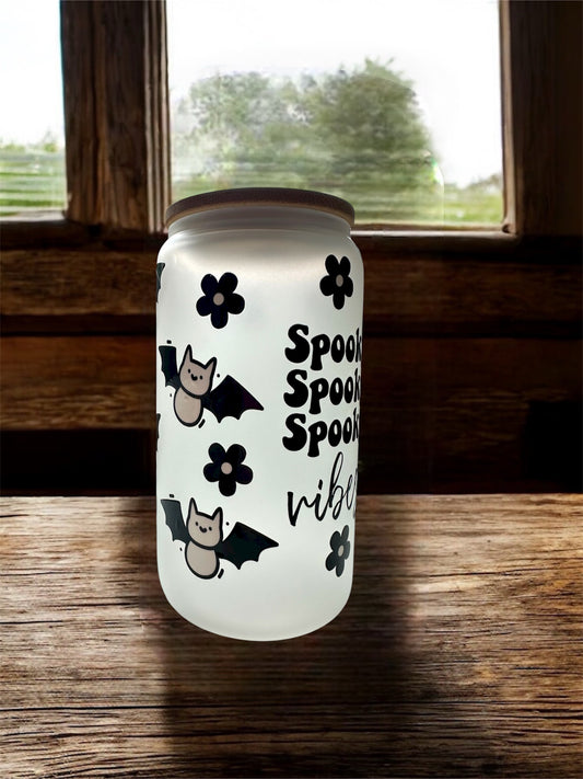 Frosted glass can-shaped tumbler with Halloween-themed design that says 'spooky spooky spooky vibes' on the front, sitting on top of a wooden surface.