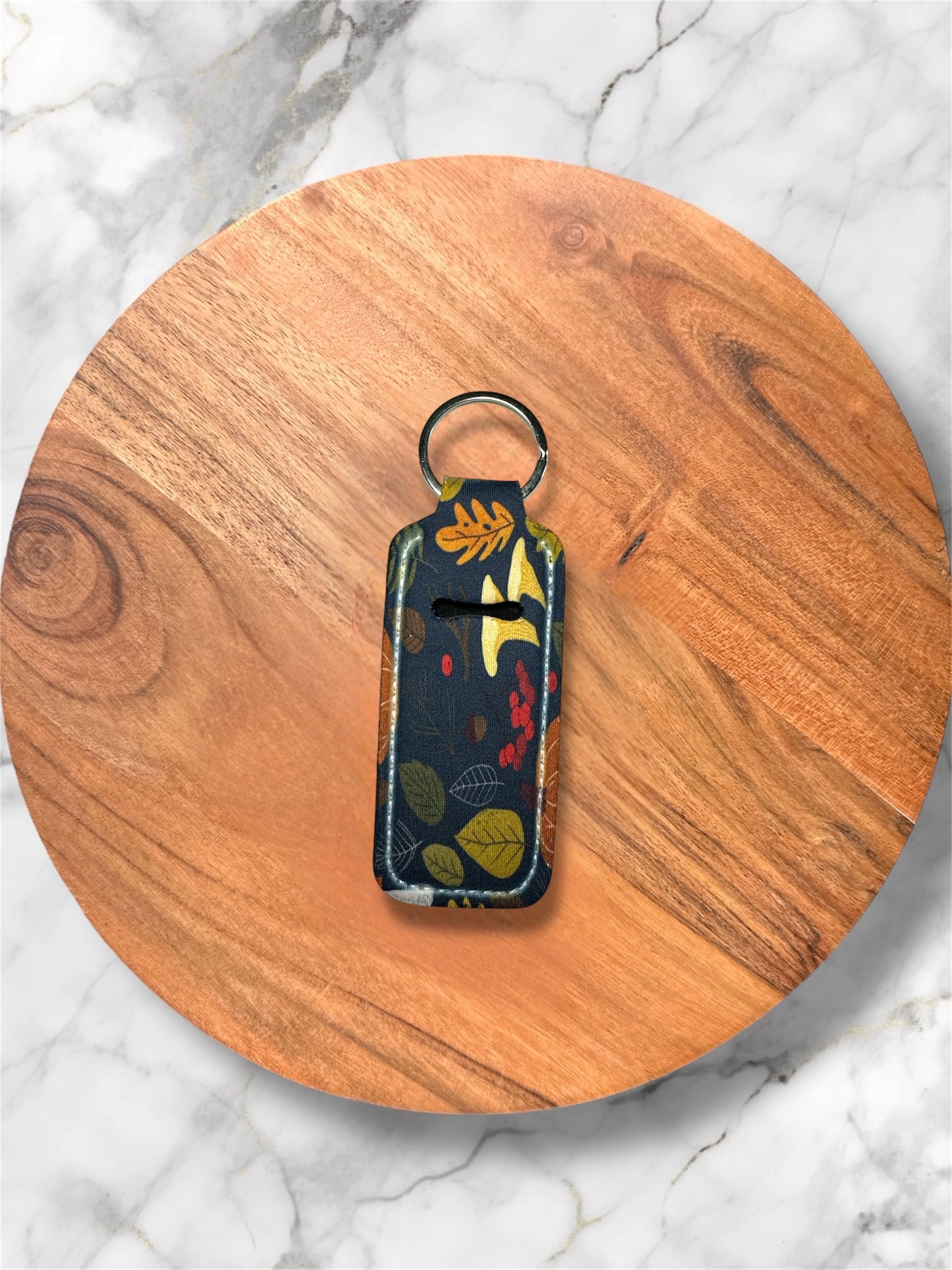 blue leaf pattern on lip balm holder keychain on wooden circle with a marble background