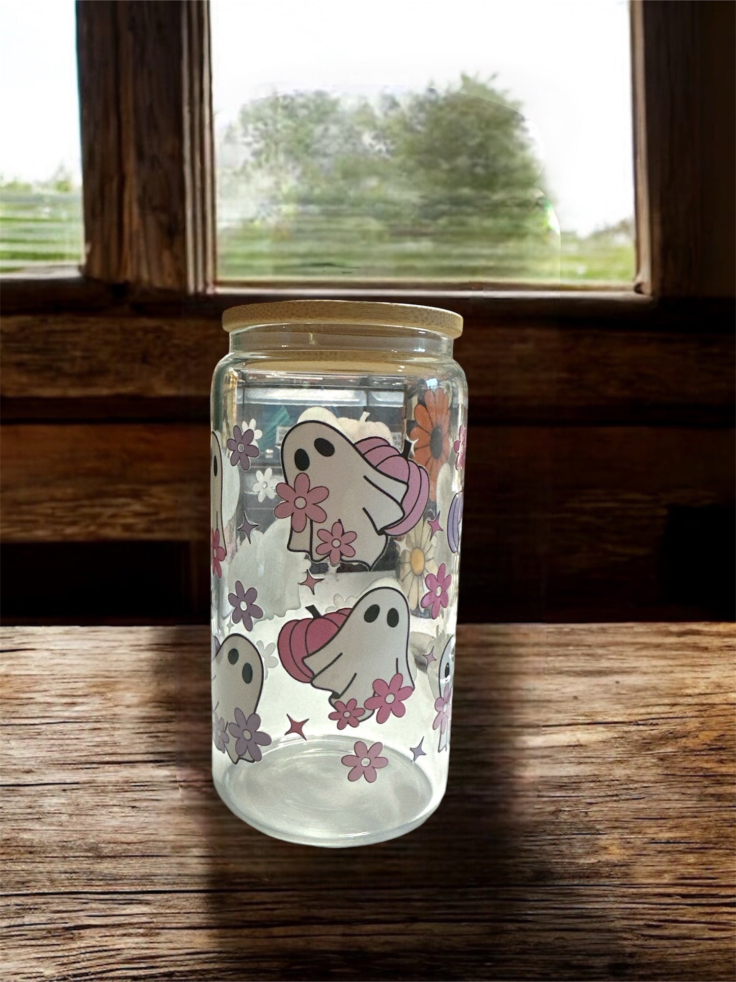 Clear 16 oz glass tumbler with wooden lid. Tumbler has ghosts with pink and purple pumpkin graphics. Tumbler is sitting on a wooden surface.