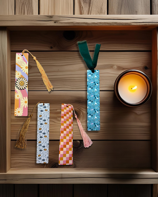 Colorful hardboard bookmarks with tassels on a wooden surface next to a lit candle.