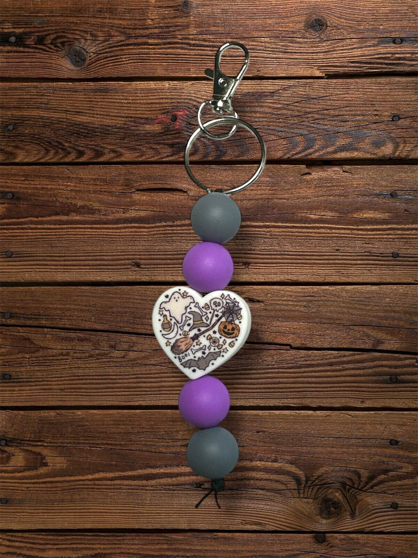 Halloween heart silicone focal bead with grey and purple silicone beads and silver keychain hardware on a wooden table