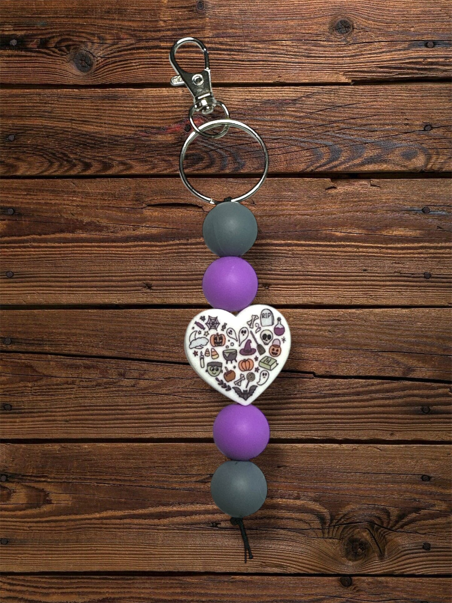Halloween heart silicone focal bead with grey and purple silicone beads and silver keychain hardware on a wooden table