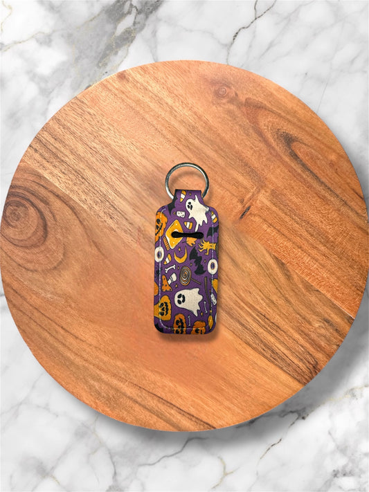 Purple Halloween-patterned lip balm keychain on a wooden surface with a marble background