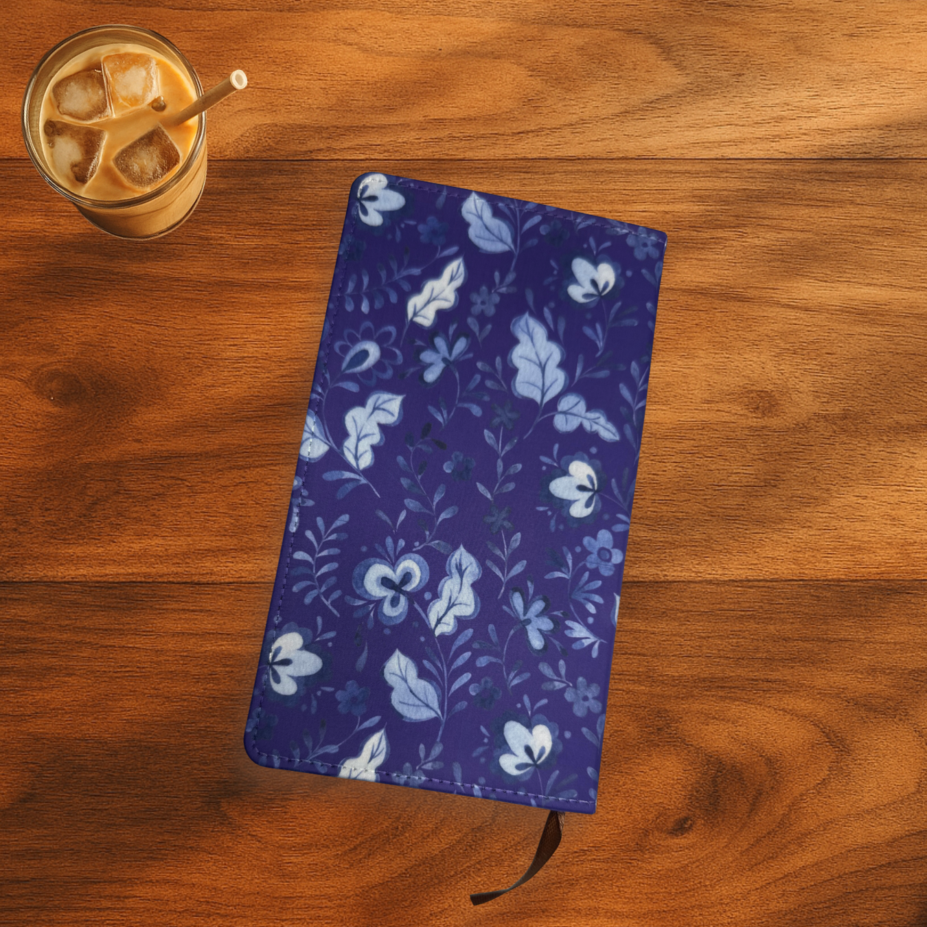 Blue floral notebook on a wooden surface with a glass of iced coffee.