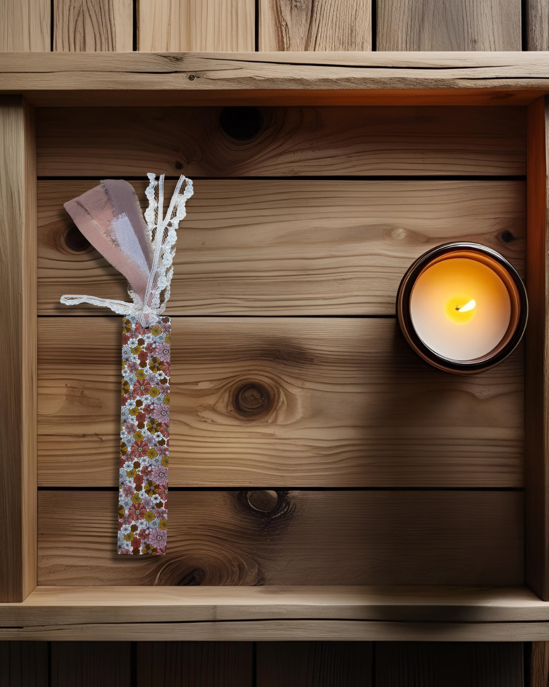 wooden background with a wildflower print hardboard bookmark next to a lit candle