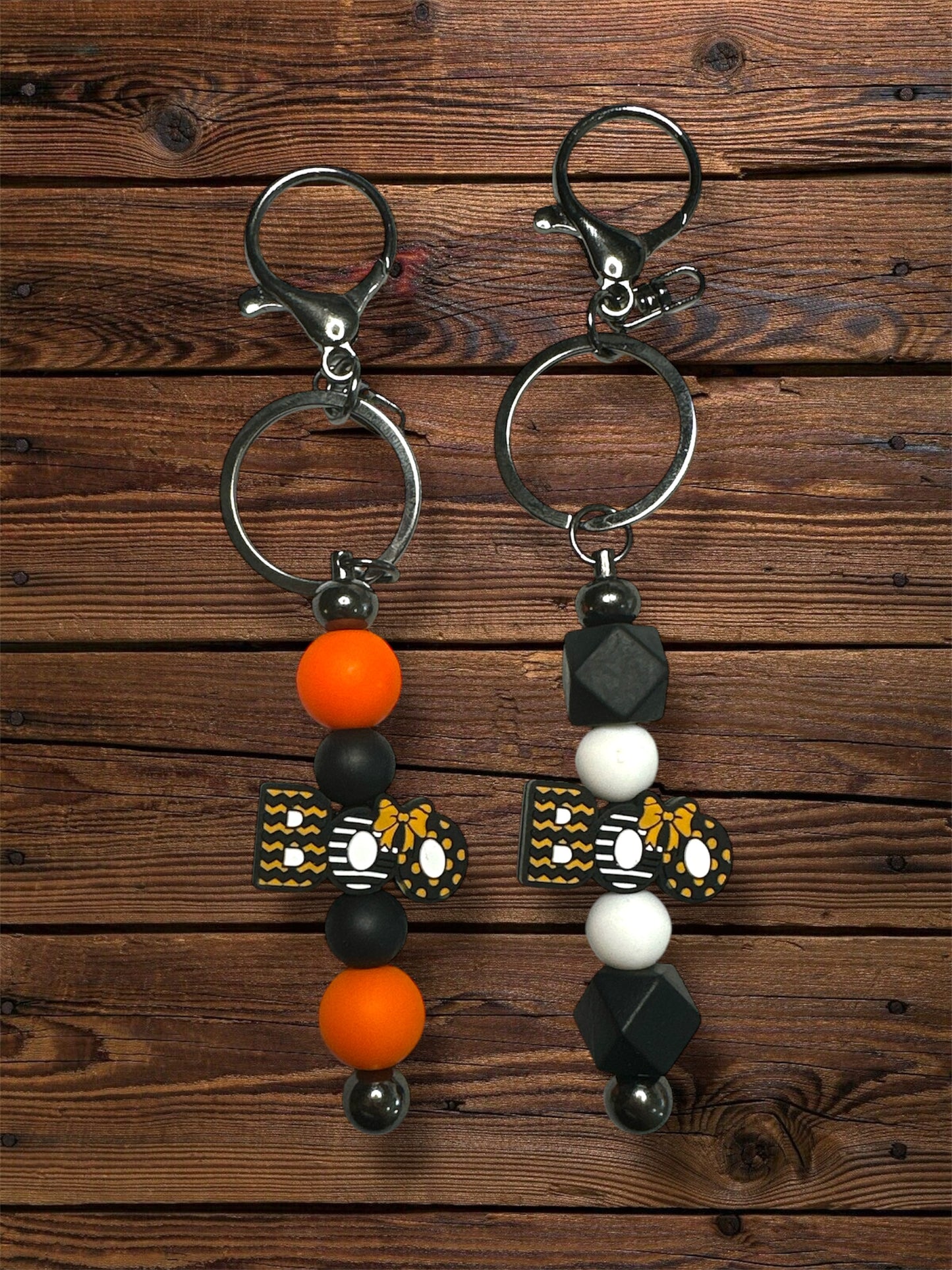 set of 2 keychains with silicone beads. both say 'boo', one has orange and white silicone beads while the other is black and orange.