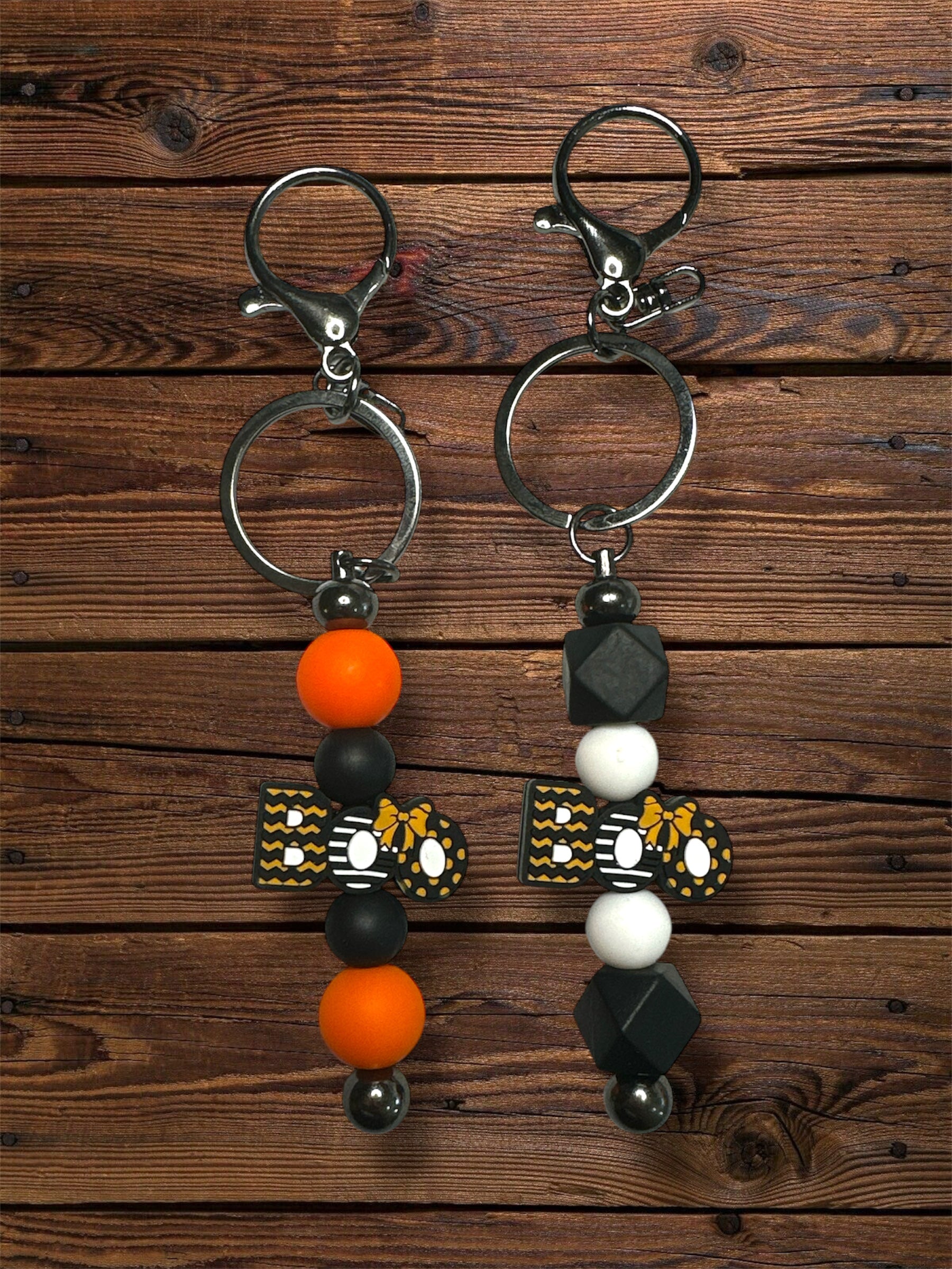 set of 2 keychains with silicone beads. both say 'boo', one has orange and white silicone beads while the other is black and orange.
