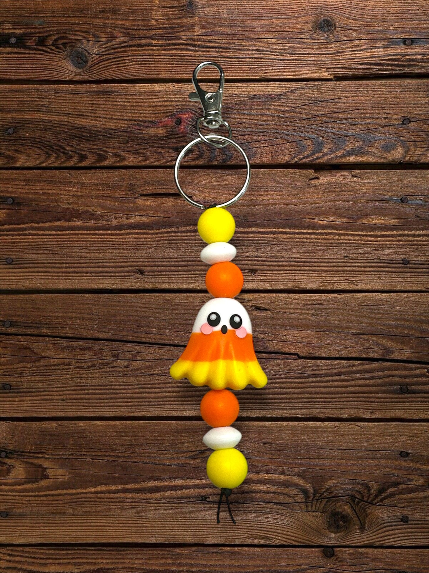 Candy corn-themed ghost silicone focal bead with a yellow and orange silicone bead with a silver keychain on a wooden background