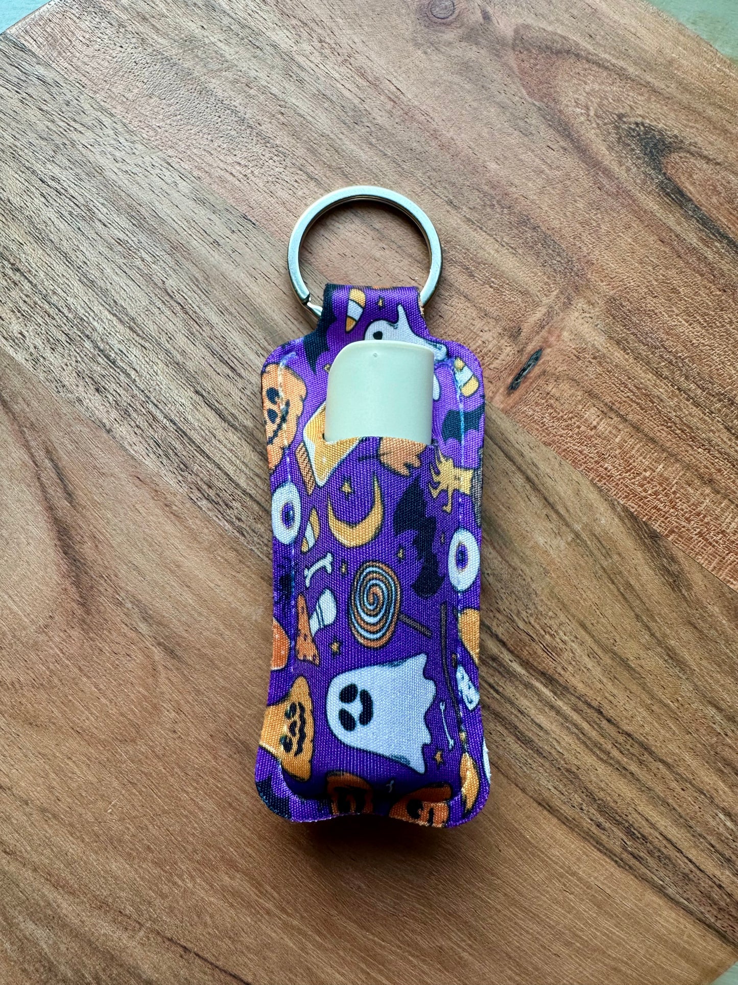 Purple Halloween-themed lip balm holder keychain on a wooden surface