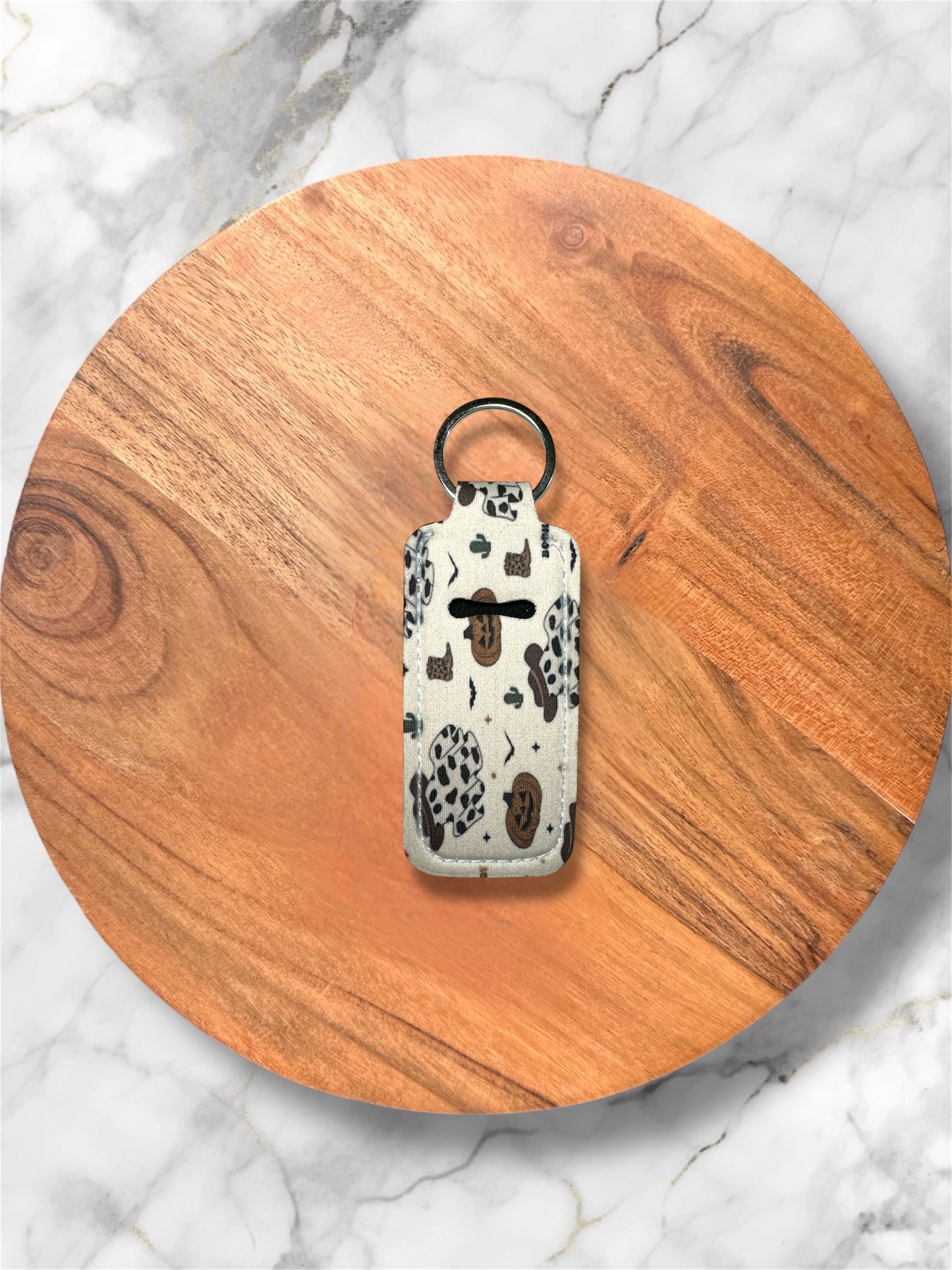 cream western pumpkin and ghost wearing cowboy hat pattern on lip balm holder keychain on a wooden circle with a marble background