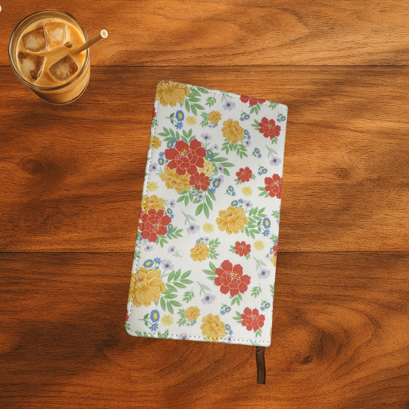 Floral polyurethane notebook with Esther 4:14 verse on the front, the notebook is on a wooden surface next to a glass of iced coffee.