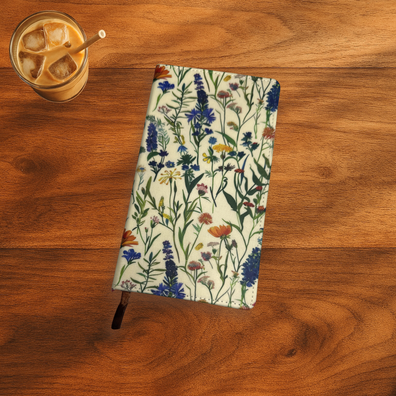 Floral print with lavender polyurethane notebook.the notebook is on a wooden surface next to a glass of iced coffee.