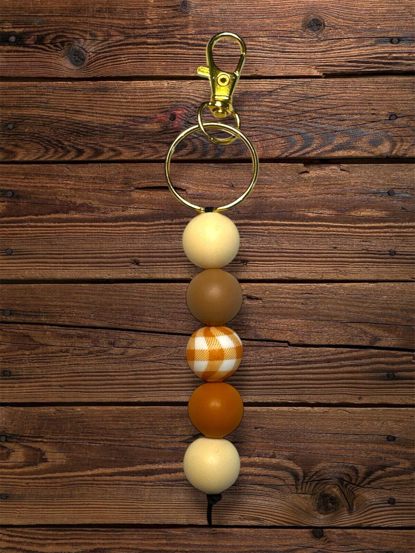 Standalone keychain with cream, brown, orange, and white gingham printed silicone beads on a wooden table