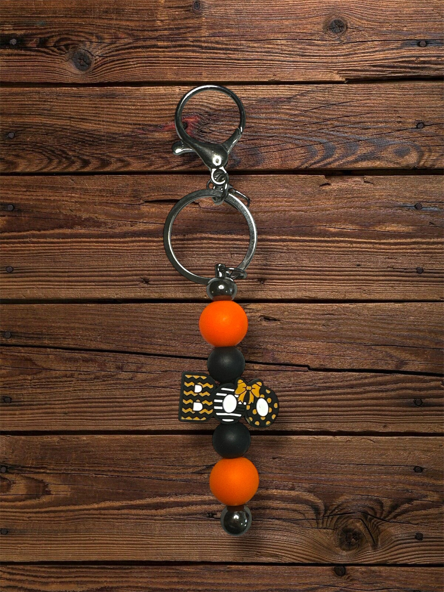 orange 'boo' silicone focal beads with orange and black beads and silver keychain hardware on a wooden table