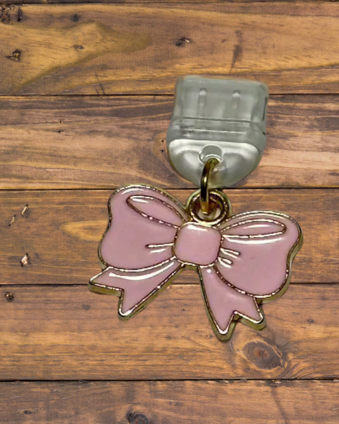 Pink bow charm with a clear dust plug on a wooden surface