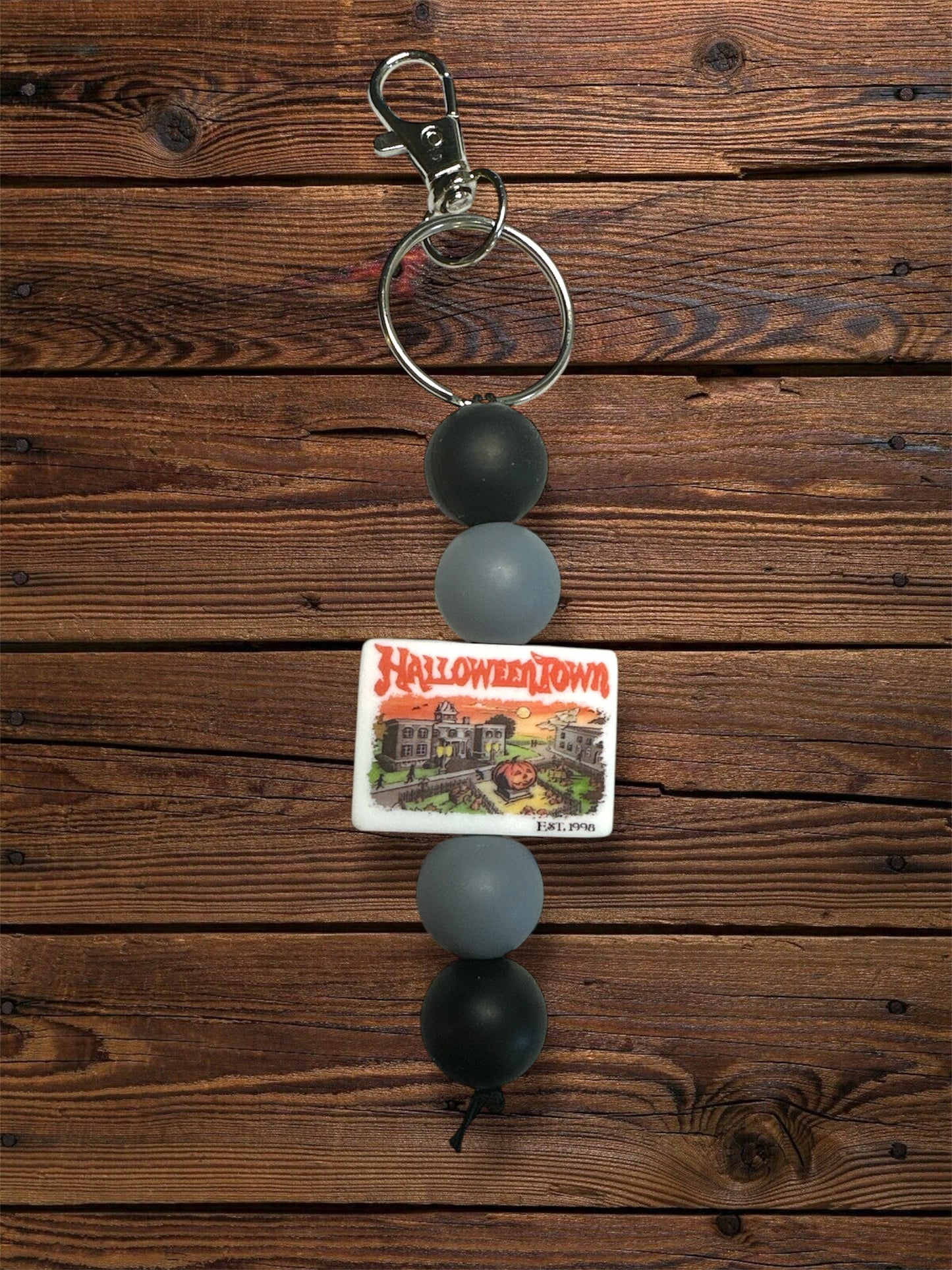 silicone 'scary town' focal bead with grey and black circular silicone beads with silver keychain hardware on a wooden table