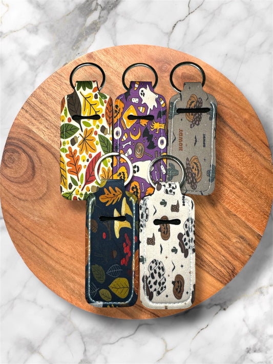 fall/ halloween themed neoprene lip balm holder keychains with silver hardware on a wooden circle with marble white and grey background
