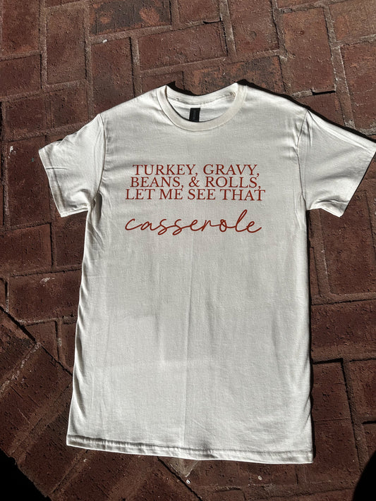 Funny Thanksgiving graphic t-shirt on natural Gildan G500 with ‘Turkey, Gravy, Beans & Rolls’ design, flat lay on brick floor.