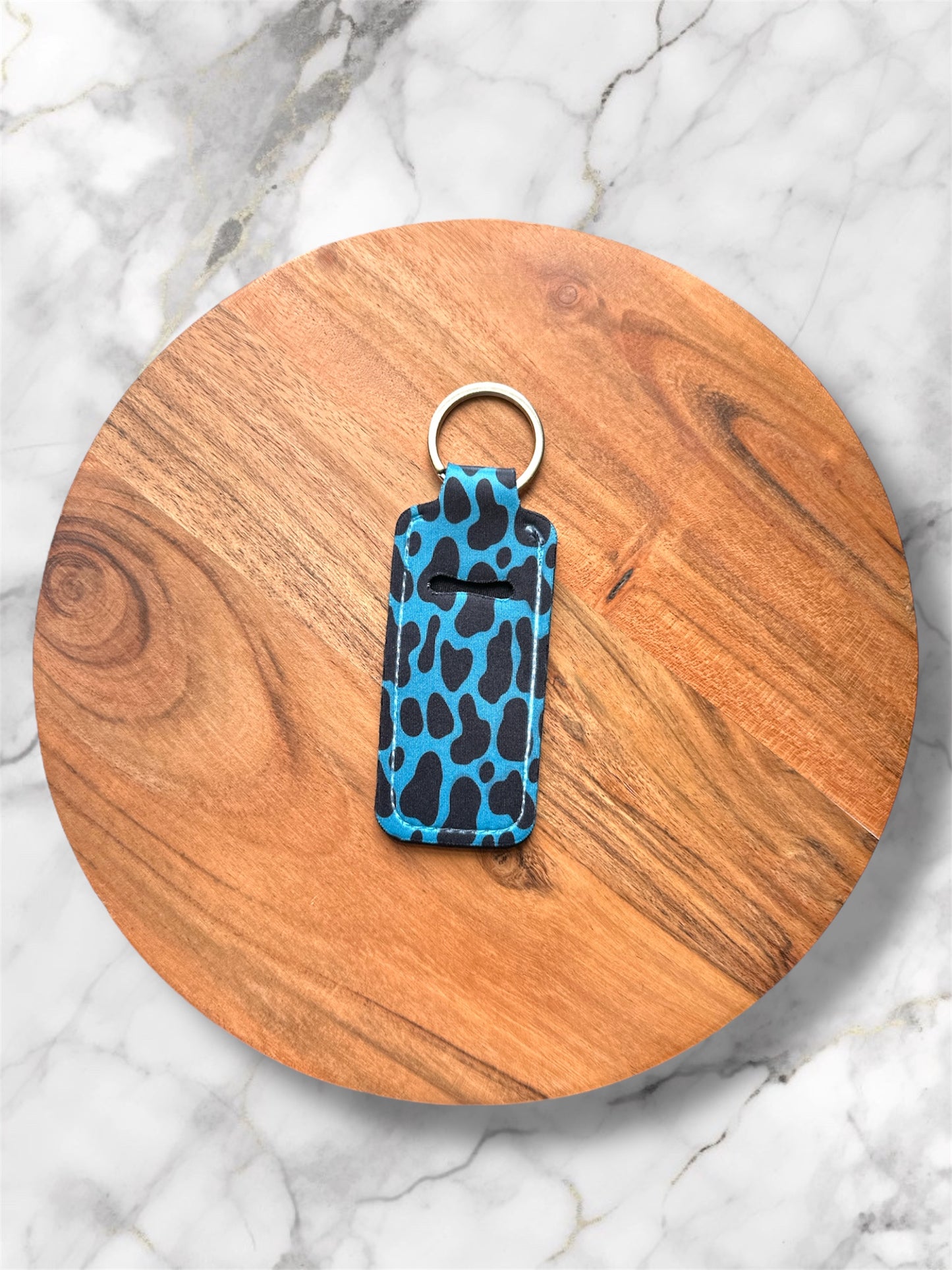 Blue cow print chapstick holder keychain on a wooden round board with a marble background