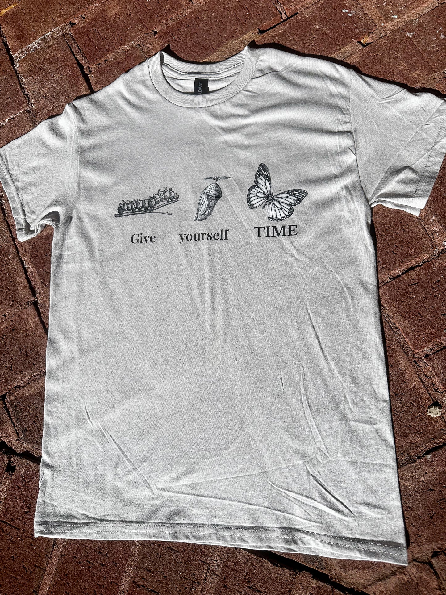 Gildan G500 ice grey unisex graphic tee with positive message displayed on brick surface