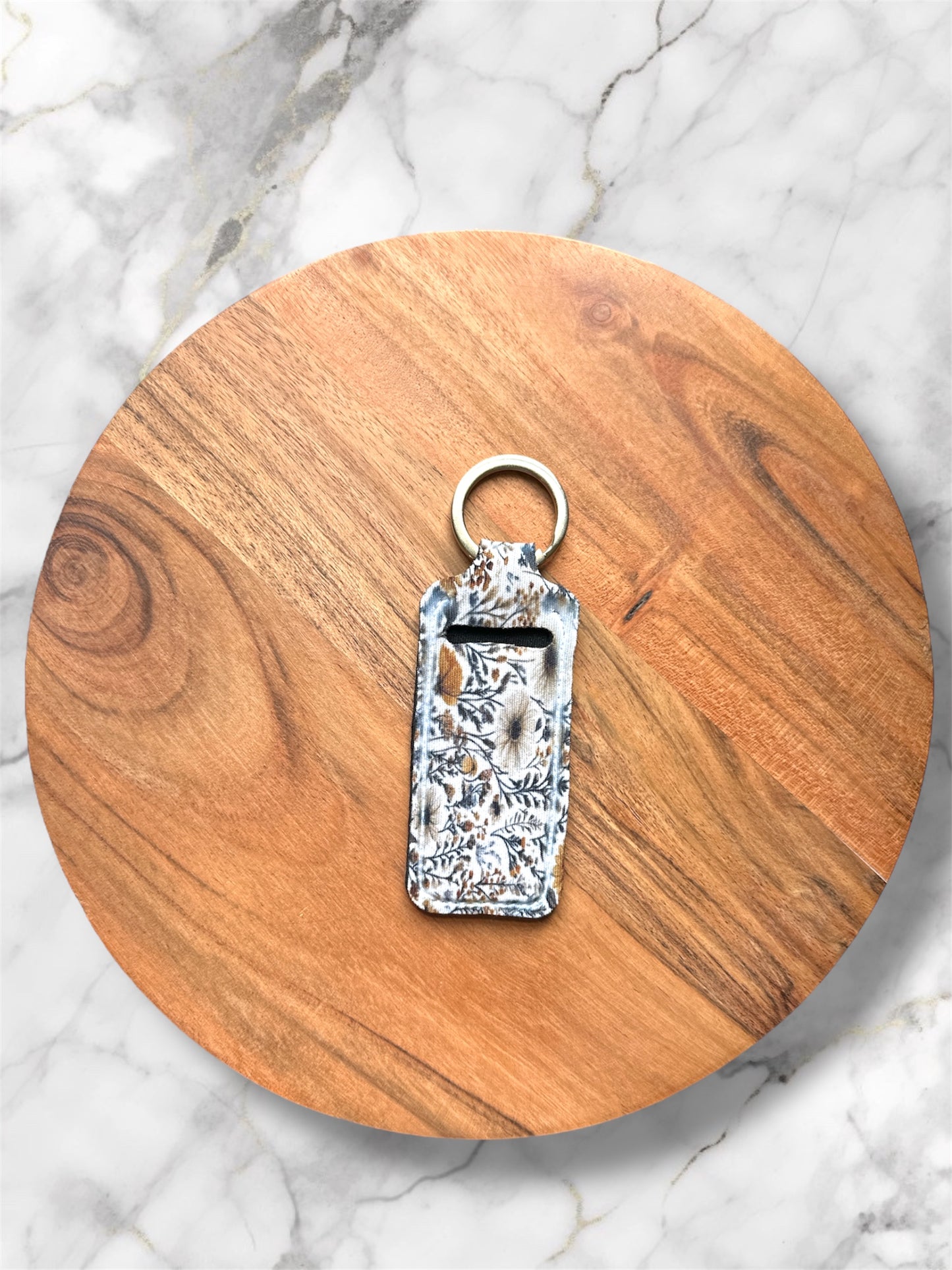 chapstick holder keychain with wildflower print on a wooden coaster with marble background