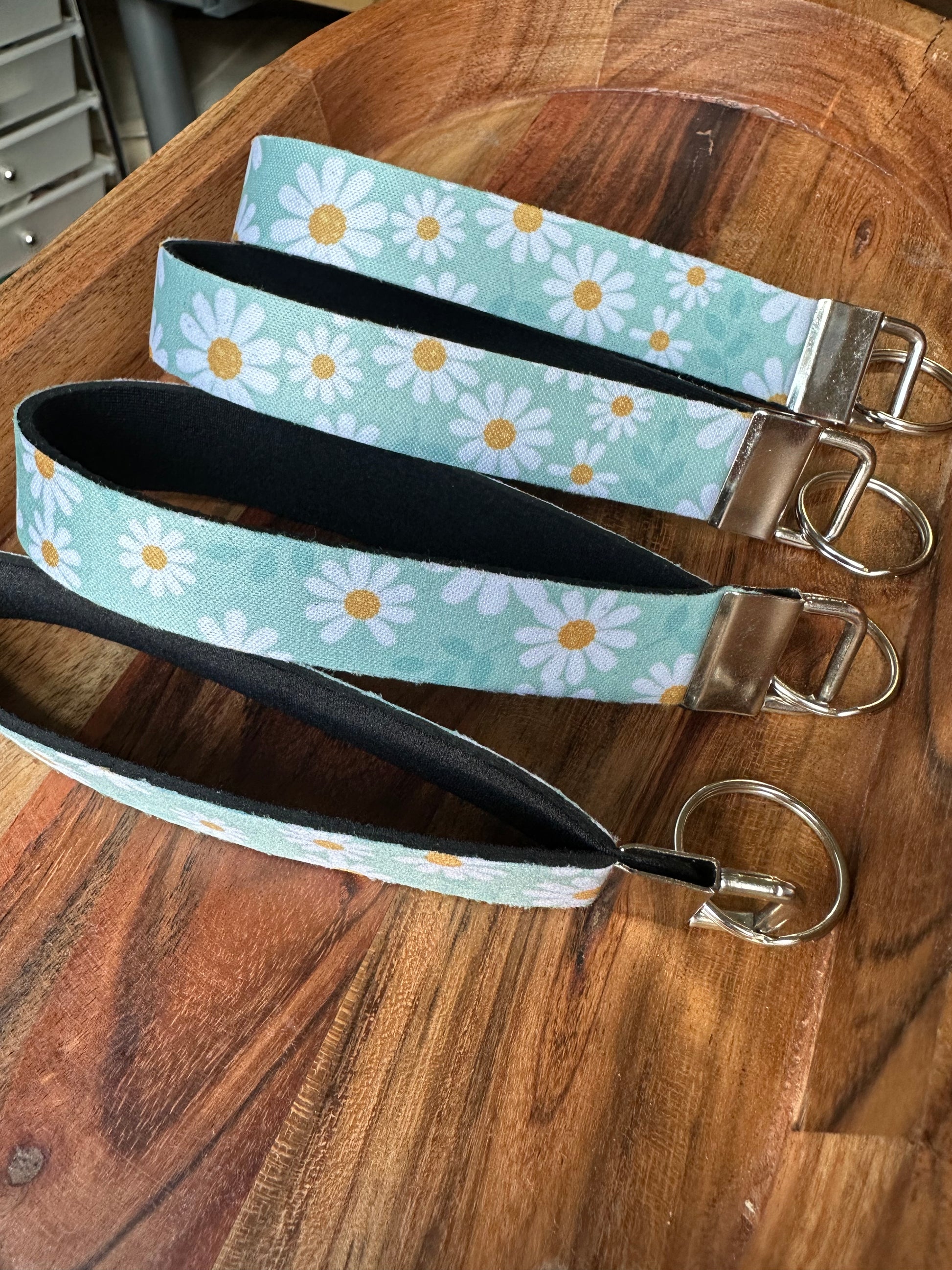 Stack of neoprene key fobs designed with a light blue background and daisies on the front