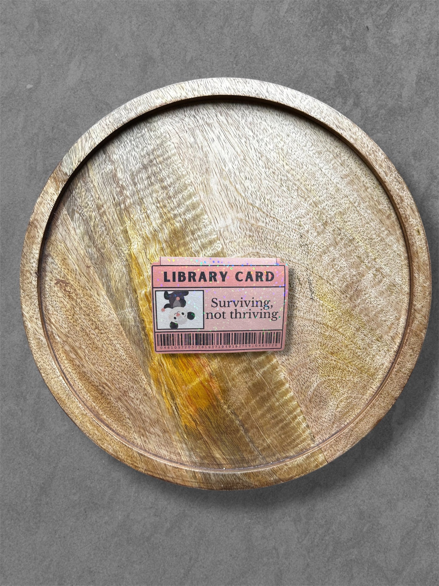 Wooden tray with a pink library card magnetic bookmark on a gray background