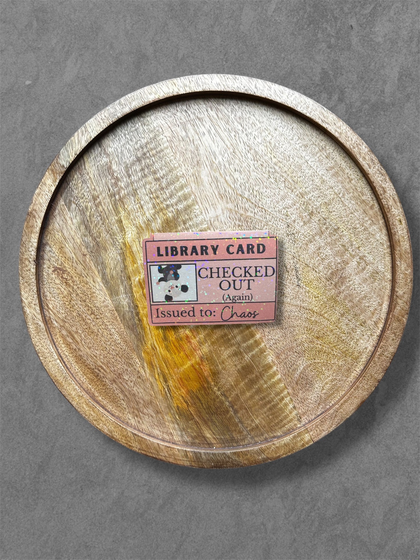 Wooden tray with a pink library card magnetic bookmark on a gray background