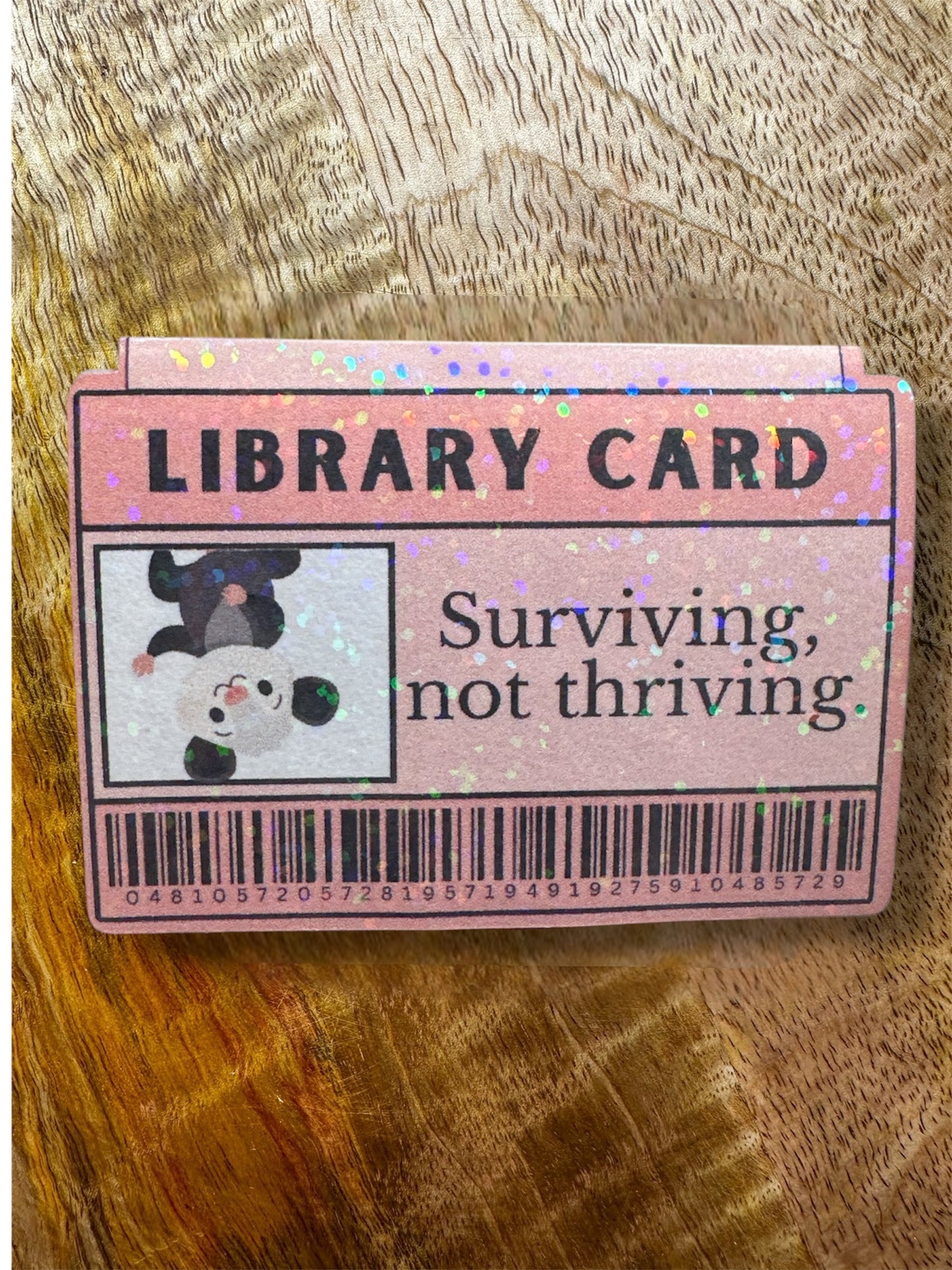 Pink library card  magnetic bookmark with text and a possum illustration on a wooden surface