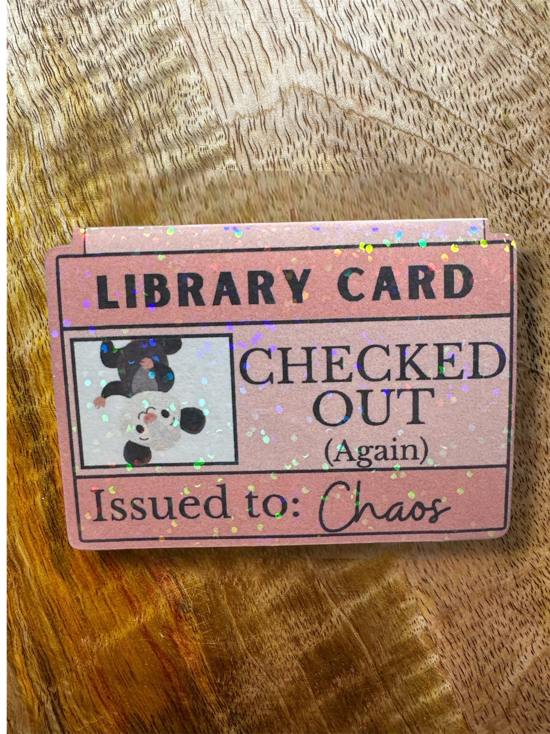 Pink library card  magnetic bookmark with text and a possum illustration on a wooden surface