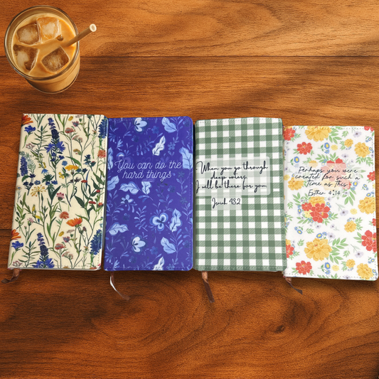 Four Sublimated polyurethane dated memo notebooks with different designs on a wooden surface next to a glass of iced coffee.