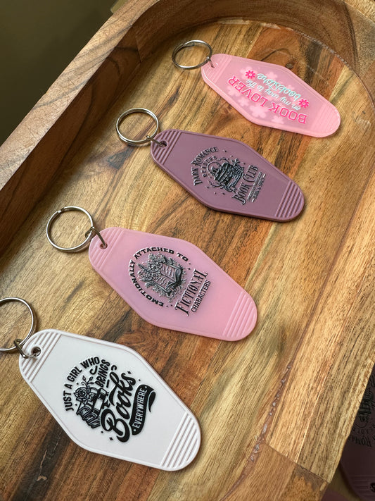 Four keychains shaped like vintage motel room keys on a wooden surface.
