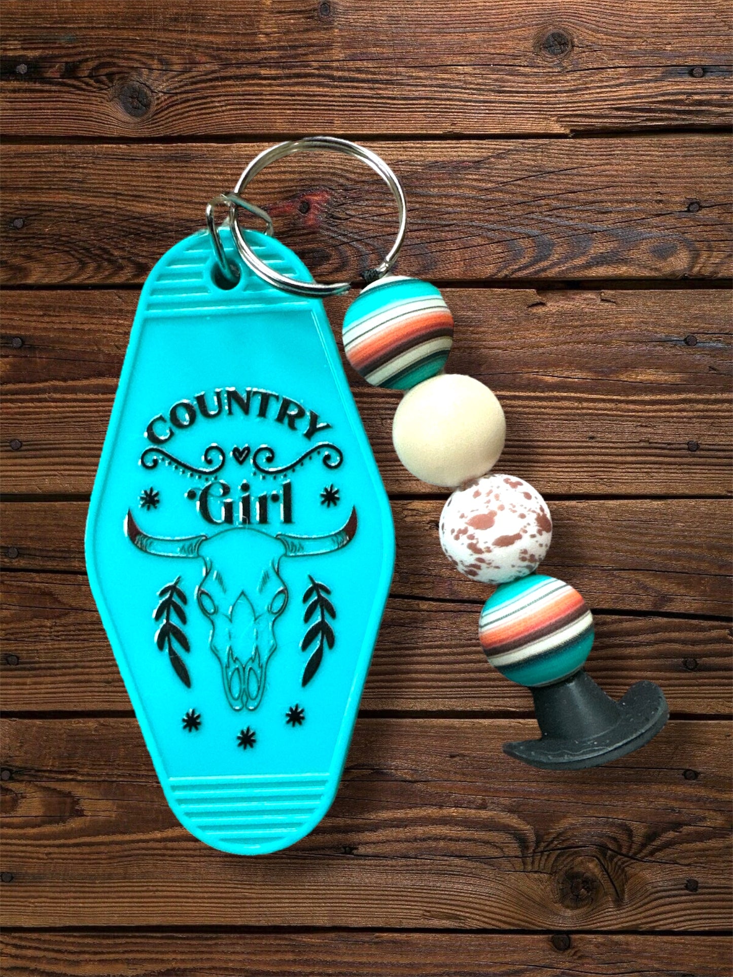 Turquoise motel keychain with 'Country Girl' design + silicone beaded keychain on a wooden surface
