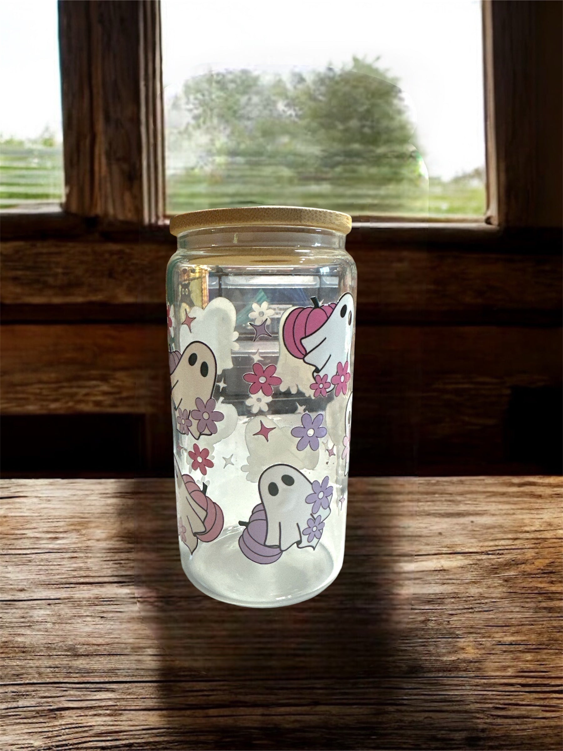 Clear 16 oz glass tumbler with wooden lid. Tumbler has ghosts with pink and purple pumpkin graphics. Tumbler is sitting on a wooden surface.